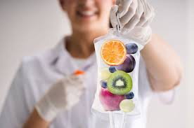 Hand holding an IV drip bag filled with fresh fruit — orange, kiwi, blueberries, grapes